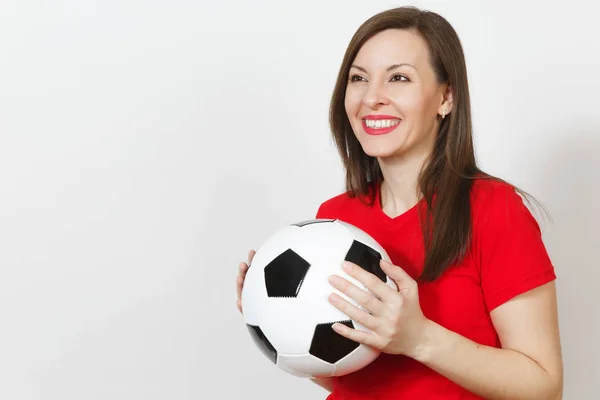 Beautiful European young cheerful happy woman, football fan or player in red uniform holding classic soccer ball isolated on white background. Sport, play football, health, healthy lifestyle concept.