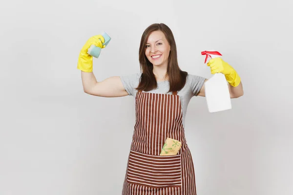 Housewife in yellow gloves, apron, cleaning rag in pocket isolated on white background. Stronge woman showing biceps muscles, holding bottle with cleaner liquid for washing dishes, sponge. Copy space. — Stock Photo, Image
