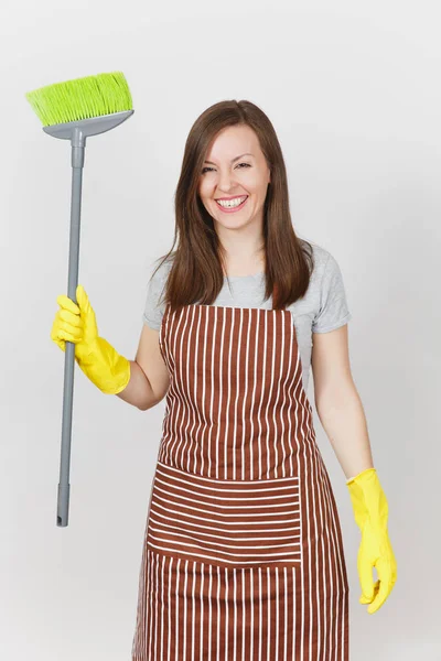 Jonge lachende huisvrouw in gestreepte schort, gele handschoenen geïsoleerd op een witte achtergrond. Huishoudster vrouw schoonmaak meid houden en vegen met bezem. Kopiëren van ruimte voor reclame. Gebied van de reclame. — Stockfoto