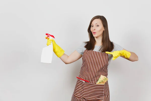 Young smiling housewife in yellow gloves, striped apron, cleaning rag, squeegee in pocket isolated on white background. Housekeeper woman holding spray bottle with cleaner liquid. Bottle copy space. — Stock Photo, Image