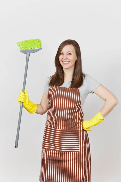 Young smiling housewife in striped apron, yellow gloves isolated on white background. Housekeeper woman cleaning maid holding and sweeping with broom. Copy space for advertisement. Advertising area. — Stock Photo, Image