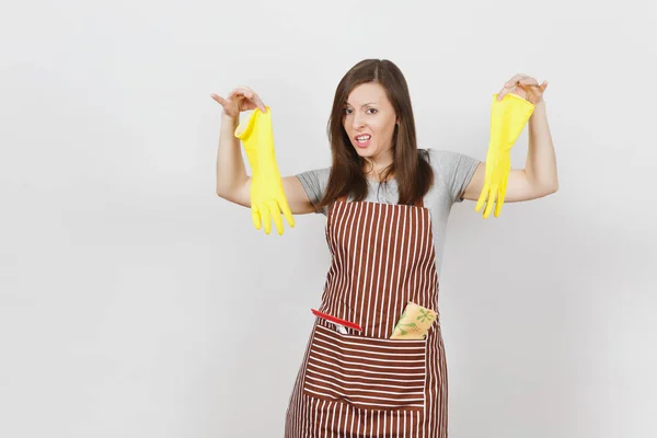 Young sad upset tired shocked housewife in striped apron with cleaning rag in pocket isolated on white background. Housekeeper woman holds smell yellow gloves in spreading hands. For advertisement. — Stock Photo, Image