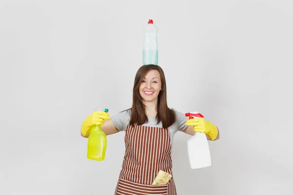 Веселая домохозяйка в жёлтых перчатках, полосатый фартук, чистка тряпки в кармане на белом фоне. Женщина держит в руках, на голове бутылки с жидкостью для мытья посуды. Копирование места для рекламы . — стоковое фото