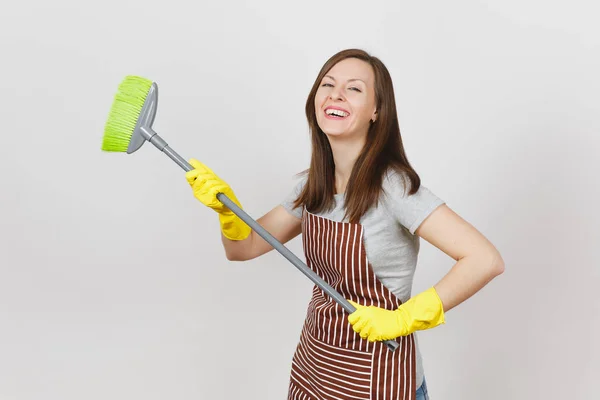 Young smiling housewife in striped apron, yellow gloves isolated on white background. Fun housekeeper woman cleaning maid holding and sweeping with broom. Copy space for advertisement Advertising area — Stock Photo, Image