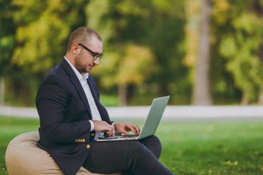 Beyaz gömlek, Klasik takım elbise, gözlük genç başarılı iş adamı. Adam dizüstü pc bilgisayar şehir Park açık havada doğa üzerinde yeşil çim üzerinde çalıştığı yumuşak kabarık üzerinde oturmak. Mobil ofis, iş kavramı.