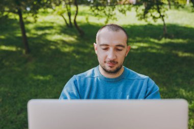 Genç başarılı akıllı adam işadamı veya açık havada çalışan öğrenci Şehir Parkı, dizüstü bilgisayar kullanarak masada oturan rahat mavi gömlekli kapatın. Mobil ofis kavramı. Kopya alanı reklam için.