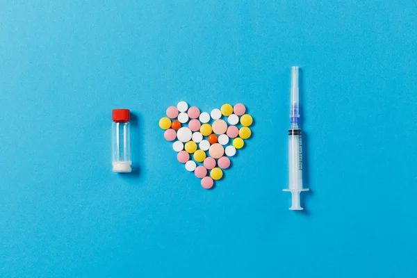 Gyógyszer-fehér, színes kerek tabletta formájában szív elszigetelt kék háttér. Tabletta, por, palack üres, fecskendő tű. Kezelés, választás egészséges életmód fogalma. Másolja a hely. — Stock Fotó