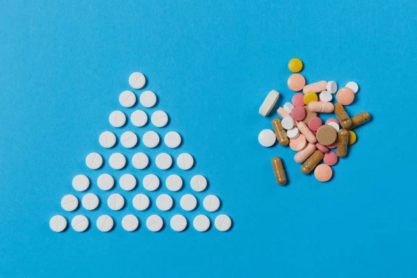 Gyógyszert fehér kerek tabletta formájában háromszög elszigetelt kék háttér rendezett. Csomó sokszínű tabletták, geometriai piramis formával. Koncepció, az egészség, kezelés, választás, egészséges életmód. — Stock Fotó
