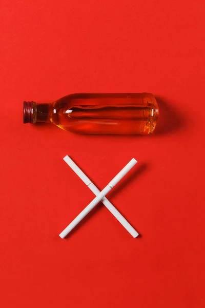 Två korsade vita cigaretter som bokstaven X, flaska med alkohol cognac, whiskey på röd bakgrund. Hälsa, val, hälsosam livsstilskoncept. Kopiera utrymme för annonseringen. Med plats för text. — Stockfoto
