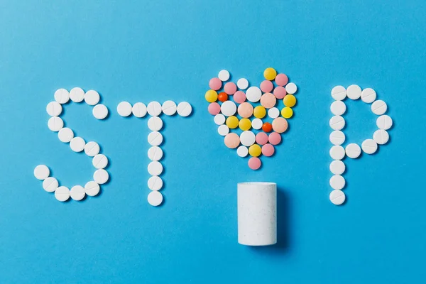 Gyógyszer-fehér, színes kerek tabletta, elszigetelt Stop Word kék háttér. Tabletták szív, alakzat, betű, üveg. Koncepció, az egészség, kezelés, választás, egészséges életmód. Másolja a hely hirdetés. — Stock Fotó