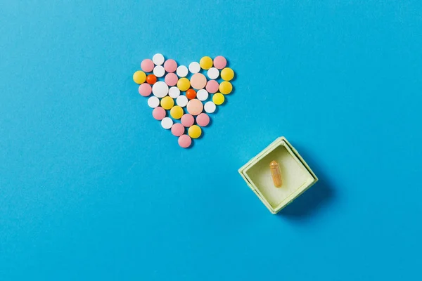 Medicamentos comprimidos redondos blancos y coloridos en forma de corazón aislado sobre fondo azul. Caja cuadrada con pastillas. Concepto de salud, tratamiento, elección, estilo de vida saludable. Espacio de copia para publicidad . — Foto de Stock