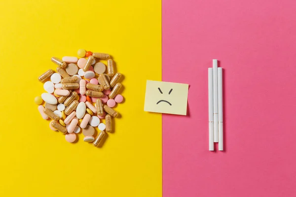 Het kleurrijke ronde medicatie witte tabletten pillen gerangschikt abstract drie sigaretten op gele kleur achtergrond. Papieren sticker vel triest glimlach gezicht. Behandeling keuze gezonde levensstijl concept. Kopiëren van ruimte. — Stockfoto