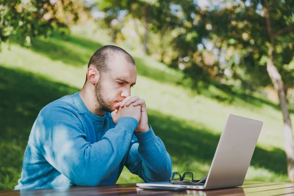 Fiatal fáradt üzletember szomorú ember, vagy diák alkalmi kék ing, szemüveg Városligetben használ laptop, mobiltelefon asztalnál ülő munka a szabadban, aggódik a problémák. Mobile Office-koncepció. — Stock Fotó