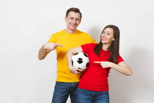 Весела усміхнена весела молода пара, жінка, чоловік, шанувальники футболу в жовтій і червоній формі підбадьорюють команду підтримки, що тримає футбольний м'яч ізольовано на білому тлі. Спорт, сімейне дозвілля, концепція способу життя . — стокове фото