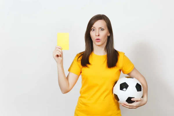 Mujer joven severa europea seria, árbitro de fútbol o jugador en uniforme amarillo mostrando tarjeta amarilla, sosteniendo pelota de fútbol aislado sobre fondo blanco. Deporte jugar al fútbol, concepto de estilo de vida saludable . —  Fotos de Stock
