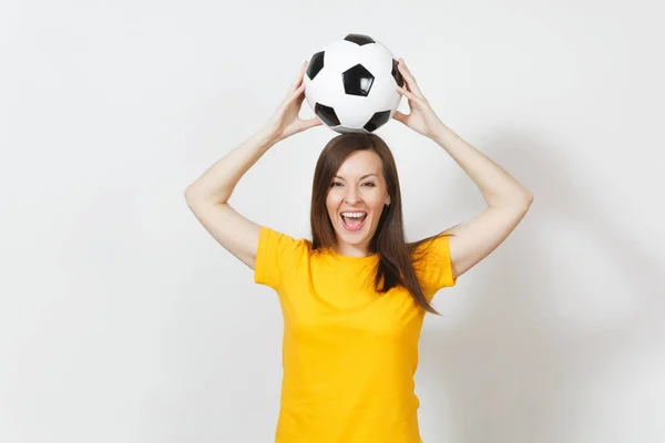 Hermosa joven europea alegre mujer, fanático del fútbol o jugador en uniforme amarillo sosteniendo por encima de la cabeza pelota de fútbol aislado sobre fondo blanco. Deporte, fútbol, salud, concepto de estilo de vida saludable . — Foto de Stock