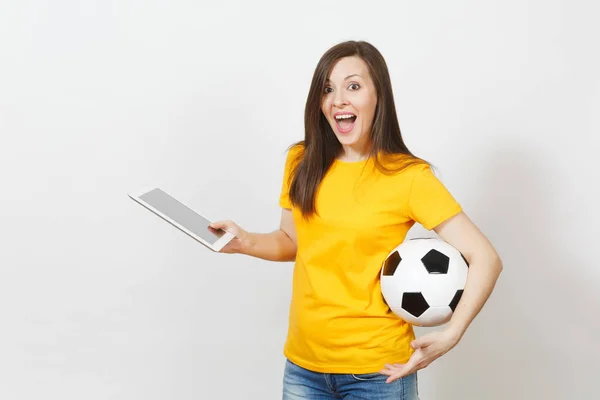 Beautiful European young cheerful woman, football fan or player in yellow uniform holding tablet pc, soccer ball isolated on white background. Sport, play football, health, healthy lifestyle concept.