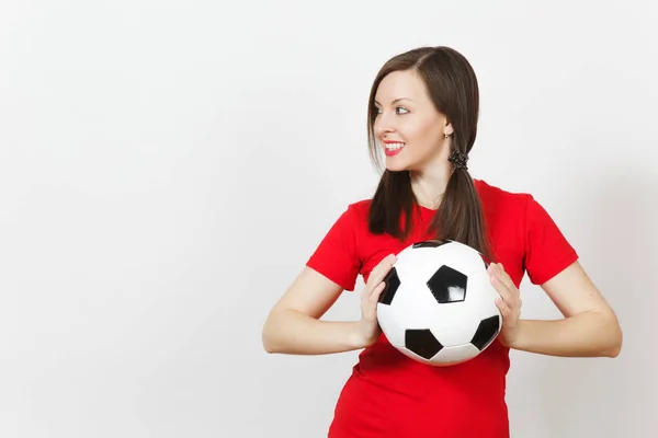Smiling European young woman, two fun pony tails, football fan or player in red uniform hold classic soccer ball isolated on white background. Sport play football, healthy lifestyle concept. Side view