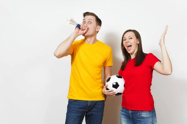 Divertida pareja joven alegre loca, mujer, hombre, aficionados al fútbol en uniforme amarillo y rojo animar equipo de apoyo con pelota de fútbol de tubo aislado sobre fondo blanco. Deportes, ocio familiar, concepto de estilo de vida . —  Fotos de Stock