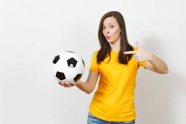 Beautiful European young cheerful happy woman, football fan or player in yellow uniform pointing on soccer ball isolated on white background. Sport, play football, health, healthy lifestyle concept.