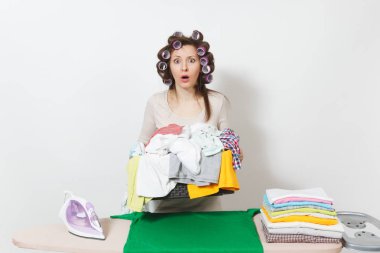 Curlers saç sepet korumasız aile giyim demir ile Ütü Masası üzerine tutarak hafif giysiler ile sıkıntılı üzgün ev kadını. Beyaz arka plan üzerinde izole kadın. Kopyalama alanı reklam.