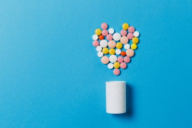İlaç beyaz, renkli yuvarlak mavi arka plan üzerinde izole kalp şeklinde tablet. Hapları geometrik şekil, şişe. Sağlık, tedavi, seçim, sağlıklı yaşam kavramı. Kopyalama alanı reklam.