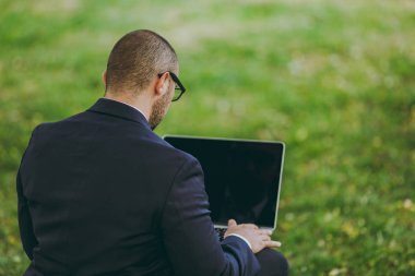 Takım, gözlük genç işadamı kapatın. Adam dizüstü pc bilgisayar şehir Park açık havada doğa üzerinde yeşil çim üzerinde çalıştığı yumuşak kabarık üzerinde oturmak. Mobil ofis, iş kavramı. Arkadan Görünüm. Kopya alanı.