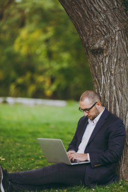 Beyaz gömlek, Klasik takım elbise, gözlük genç başarılı iş adamı. Adam çimen yere otur, dizüstü pc bilgisayar şehir Park açık havada doğa üzerinde yeşil çim üzerinde çalışmak. Mobil ofis, iş kavramı.