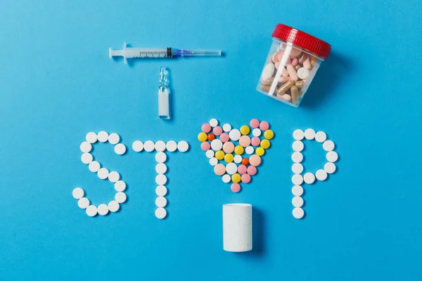 Лекарства белые, красочные круглые таблетки в слове Стоп изолированы на синем фоне. Таблетки для ампул сердца шприц с иглой. Концепция здоровья, лечения, выбора, здорового образа жизни. Для рекламы — стоковое фото