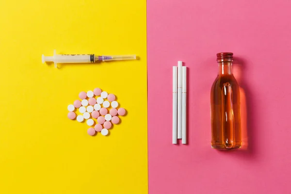 Medicinering färgglada runda tabletter piller ordnade abstrakt, Tom spruta nål flaska alkohol, cigaretter på gul rosa ros bakgrund. Behandling val hälsosam livsstil. Kopiera utrymme annons. — Stockfoto