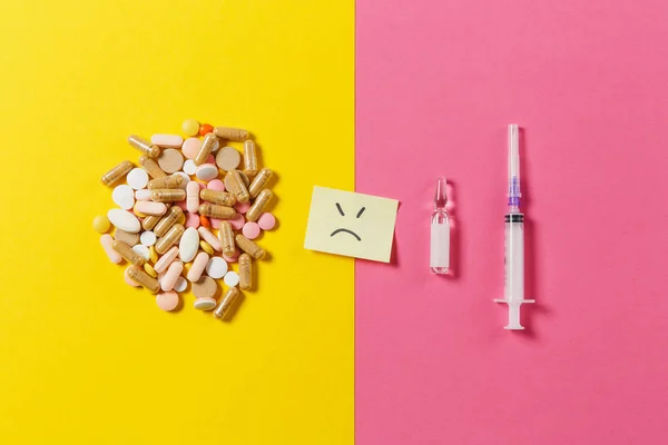 Medicatie kleurrijke tabletten, pillen geregeld abstract op geel roze achtergrond. Aspirine, ampul leeg spuit-naald, papieren sticker vel triest glimlach gezicht. Behandeling keuze, gezonde levensstijl concept. — Stockfoto