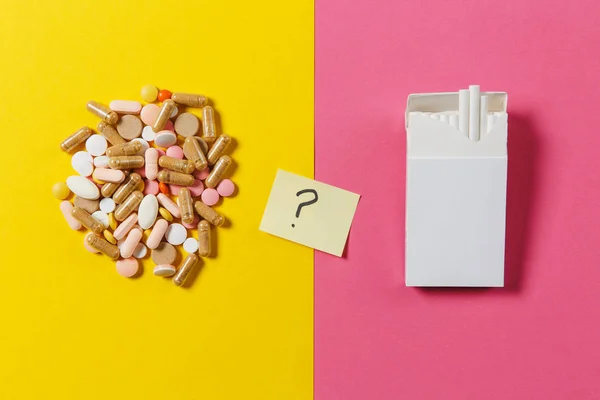 Medicatie wit kleurrijke ronde tabletten geregeld abstracte witte pack sigaretten op gele kleur achtergrond. Papieren sticker vel vraagteken. Behandeling keuze gezonde levensstijl concept. Kopiëren van ruimte. — Stockfoto