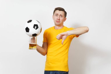 Üzgün üzgün genç Avrupa adam şaşkın, fan veya oyuncu sarı üniforma gösterisinde aşağı başparmak, bira kupa bira, beyaz arka plan üzerinde izole futbol topu tut. Spor, futbol, yaşam kavramı.