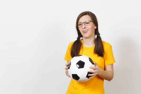 European young sad upset woman, two fun pony tails, football fan or player in glasses, yellow uniform hold classic soccer ball isolated on white background. Sport, play, football, healthy lifestyle co