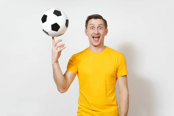 Вдохновленный молодой веселый европейский человек, фанат или игрок в желтой форме вращать футбольный мяч на пальце, приветствовать любимую футбольную команду изолированы на белом фоне. Спорт, футбол, концепция образа жизни . — стоковое фото
