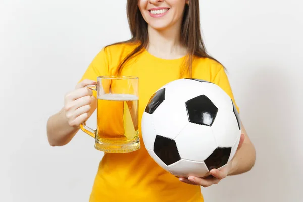 Close up cropped European young woman, football fan or player in yellow uniform holding pint mug of beer, soccer ball isolated on white background. Sport, play football, healthy lifestyle concept.