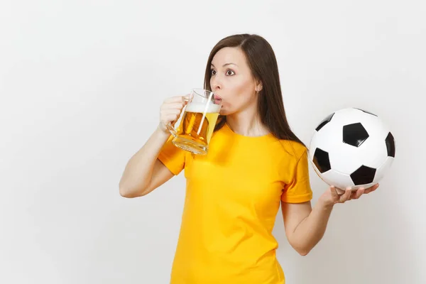 Hermosa joven europea alegre mujer, fanático del fútbol o jugador en uniforme amarillo sosteniendo jarra de cerveza, pelota de fútbol aislado sobre fondo blanco. Deporte, jugar al fútbol, concepto de estilo de vida saludable . — Foto de Stock