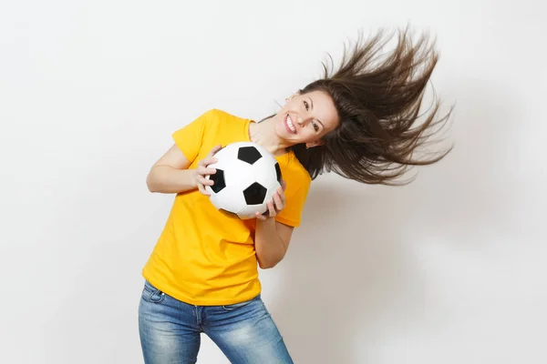 Beautiful European young woman, football fan or player in yellow uniform holding soccer ball fluttering hair isolated on white background. Sport, play football, health, healthy lifestyle concept.