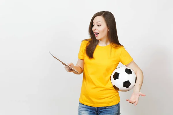 Beautiful European young cheerful woman, football fan or player in yellow uniform holding tablet pc, soccer ball isolated on white background. Sport, play football, health, healthy lifestyle concept.