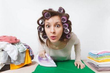 Eğlenceli yakın curlers saç ışık elbise giyim Ütü Masası üzerine demir ile Ütü ile genç ev hanımı. Beyaz arka plan üzerinde izole kadın. Temizlik kavramı. Kopya alanı reklam için.