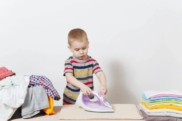 Ευτυχισμένος αγοράκι σιδερώματος ρούχων για την οικογένεια στην σιδερώστρα με σίδερο. Παιδί που βοηθούν με τις δουλειές του σπιτιού που απομονώνονται σε λευκό φόντο. Ενθάρρυνση της αυτονομίας στην αντίληψη των παιδιών. Αντίγραφο χώρος για διαφήμιση. — Φωτογραφία Αρχείου