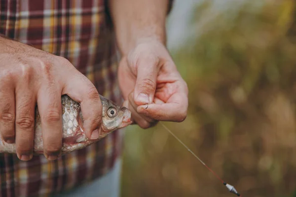 Stäng upp Man i rutig skjorta tar bort fångad fisk från en krok på ett fiskespö på en suddig pastell brun bakgrund. Livsstil, rekreation, fisherman fritid koncept. Kopiera utrymme för reklam. — Stockfoto