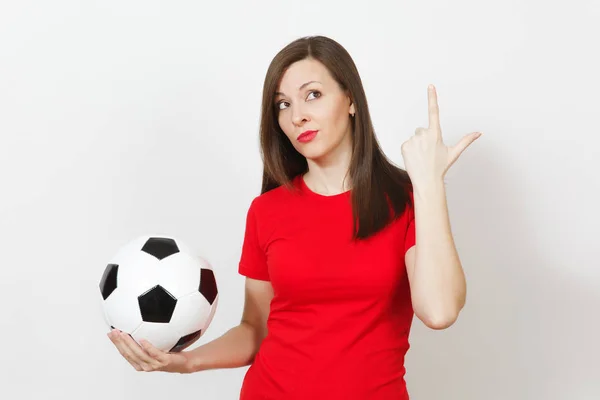 Pretty European young pensive thoughtful woman, football fan or player in red uniform holding classic soccer ball isolated on white background. Sport, play football, health, healthy lifestyle concept.