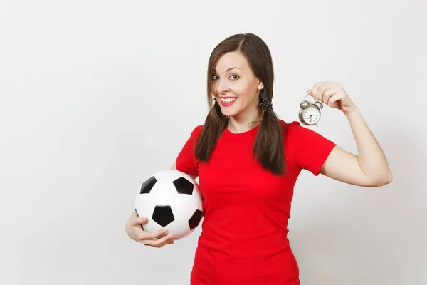 European young woman, two fun pony tails, football fan or player in red uniform hold old alarm clock, soccer ball isolated on white background. Sport play football health, time lifestyle concept.