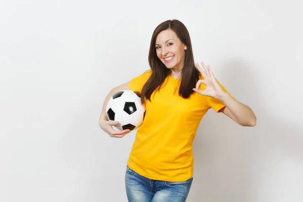 Hermosa joven europea, fanática del fútbol o jugadora en uniforme amarillo sosteniendo pelota de fútbol mostrando gesto OK aislado sobre fondo blanco. Deporte, fútbol, salud, concepto de estilo de vida saludable . — Foto de Stock