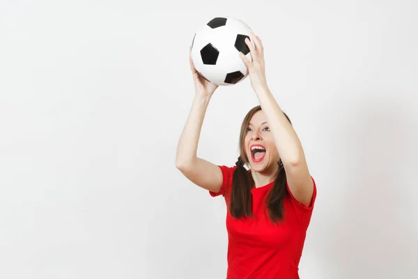 Mujer joven europea activa, dos divertidas colas de caballo, fanático del fútbol o jugador en uniforme rojo atrapando pelota de fútbol clásico aislado sobre fondo blanco. Deporte jugar fútbol salud, concepto de estilo de vida saludable . — Foto de Stock