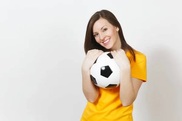 Hermosa joven europea alegre mujer feliz, fanático del fútbol o jugador en uniforme amarillo abrazando pelota de fútbol aislado sobre fondo blanco. Deporte, fútbol, salud, concepto de estilo de vida saludable . — Foto de Stock