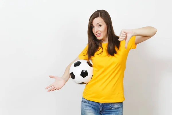 Bastante europeo joven triste mujer molesta, fanático del fútbol o jugador en uniforme amarillo sosteniendo pelota de fútbol, mostrando el pulgar hacia abajo aislado sobre fondo blanco. Deporte, jugar al fútbol, concepto de estilo de vida saludable . — Foto de Stock