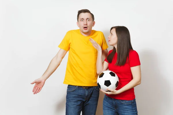 Sad upset young couple, woman, man, football fans in yellow red uniform with soccer ball cheer up team worries about losing team isolated on white background. Sport, family leisure, lifestyle concept.