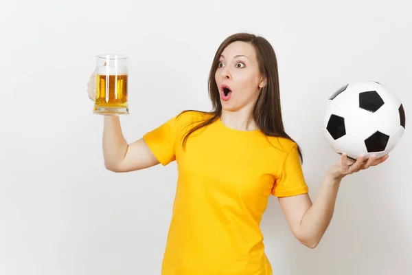 Beautiful European young cheerful woman, football fan or player in yellow uniform holding pint mug of beer, soccer ball isolated on white background. Sport, play football, healthy lifestyle concept.